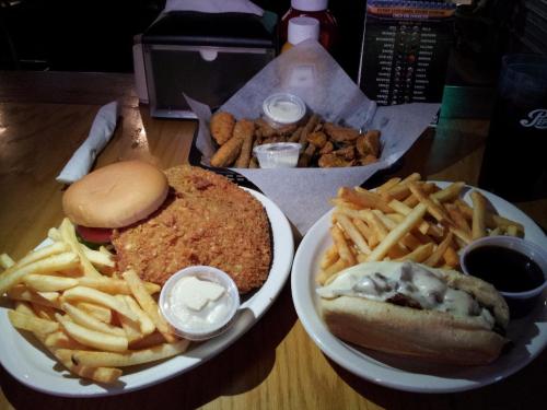 A plate of crispy fried chicken sandwich with fries, and a side of chicken tenders and more fries on a wooden table.