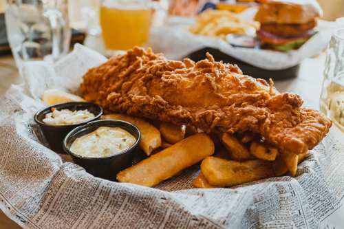 A plate of crispy fried fish served with golden fries and two dipping sauces on a bed of newspaper.