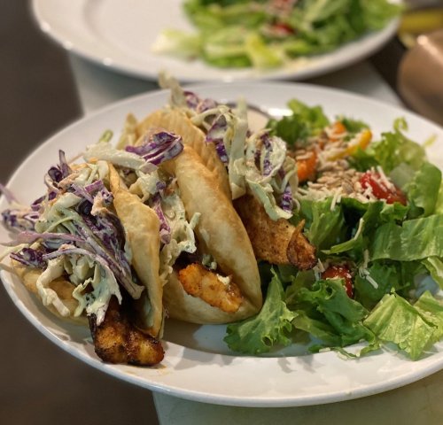 Two fish tacos topped with cabbage slaw, served with a side salad of mixed greens and colorful vegetables.