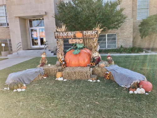 A festive display featuring a large pumpkin, hay bales, and scarecrows, celebrating "Punkin' Days 2019" outdoors.