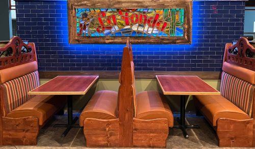 Two wooden booths with tables in a restaurant, featuring a colorful stained glass sign above.