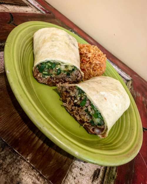 A plate with two burritos filled with meat and green onions, accompanied by a serving of rice.