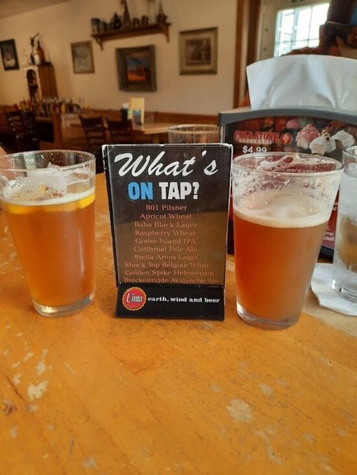 Two glasses of beer sit on a table next to a menu titled "What's On Tap," featuring various beer options.