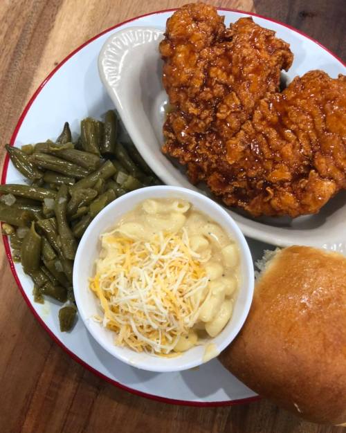 A plate featuring two crispy fried chicken pieces, green beans, macaroni and cheese topped with cheese, and a dinner roll.