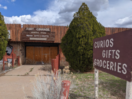 Abandoned general store with wooden signage, surrounded by trees and a sign for curios, gifts, and groceries.
