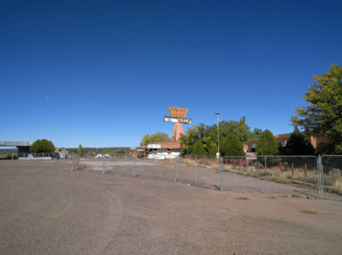 Abandoned building with a large sign reading "Vacancy" under a clear blue sky, surrounded by a fenced area.