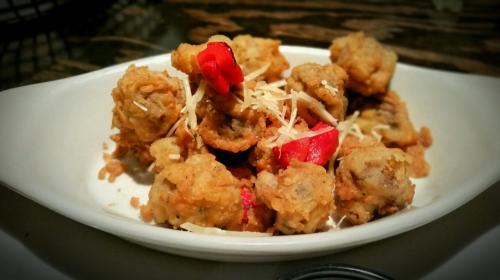 A plate of crispy fried mushrooms topped with red peppers and grated cheese.