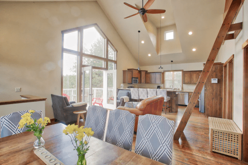Bright, modern interior of a cozy cabin with a dining area, kitchen, and large windows showcasing a scenic view.