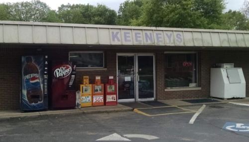 A small store named "Keeneys" with vending machines and a newspaper stand, surrounded by greenery.