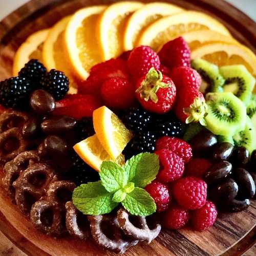 A colorful fruit platter featuring oranges, strawberries, raspberries, blackberries, kiwi, and chocolate-covered pretzels.