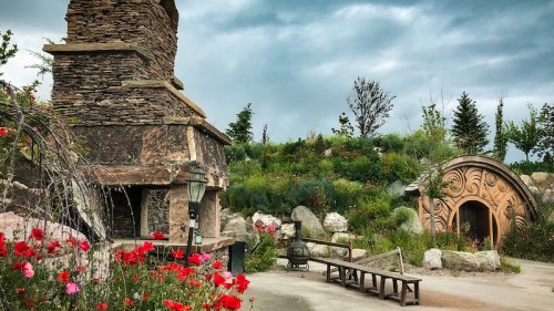 A scenic garden with stone structures, colorful flowers, and a cloudy sky, creating a tranquil outdoor setting.