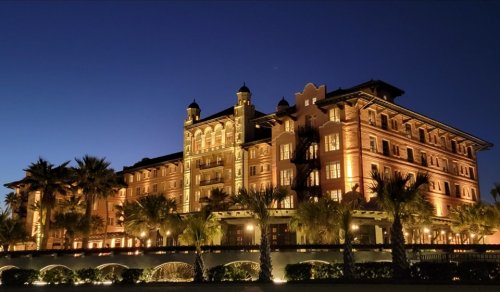 A beautifully lit historic hotel at dusk, surrounded by palm trees and a clear sky.