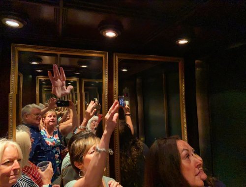A crowded elevator with people taking photos, surrounded by mirrors reflecting their images.