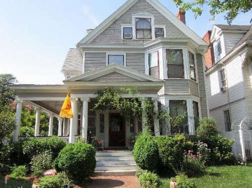A charming Victorian-style house with a porch, surrounded by lush greenery and colorful flowers.