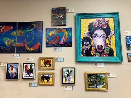 A colorful gallery wall featuring various animal-themed paintings, including cows, roosters, and abstract fish art.