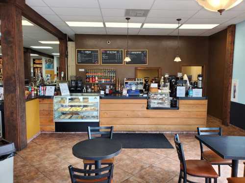 A cozy café interior featuring a service counter, display case, and seating area with tables and chairs.