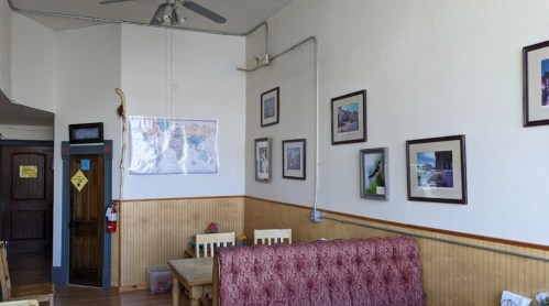 Cozy café interior with wooden tables, a map on the wall, and framed photos, creating a warm atmosphere.