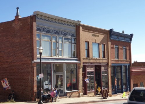 Historic brick buildings line a street, featuring shops and outdoor seating under a clear blue sky.