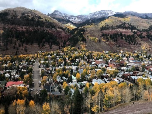 A scenic view of a mountain town surrounded by autumn foliage and snow-capped peaks in the background.