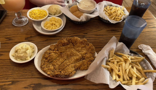 A plate of fried chicken with sides of mashed potatoes, macaroni, corn, and fries, alongside drinks and rolls.
