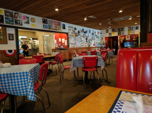 A cozy diner with checkered tablecloths, red chairs, and walls adorned with posters and decorations.