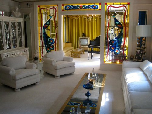 A bright living room featuring white furniture, a glass coffee table, and colorful stained glass windows.
