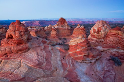Colorful rock formations with layered textures under a clear blue sky, showcasing natural beauty in a desert landscape.