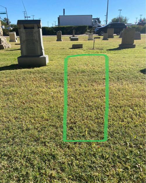 A grassy area in a cemetery with a green outline indicating a grave marker location.