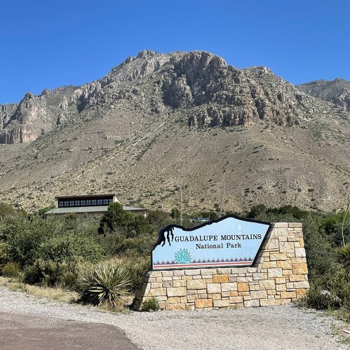 Sign for Guadalupe Mountains National Park with mountains in the background and clear blue sky.