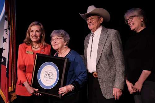 A group of four people, including a woman holding an award, pose together with a flag in the background.