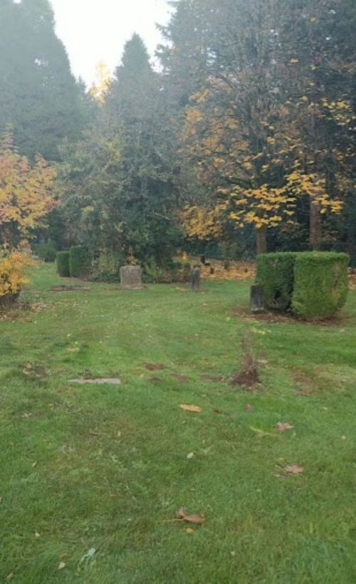 A serene graveyard with gravestones surrounded by trees and colorful autumn foliage.