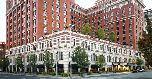 Historic brick hotel building with a modern facade, featuring greenery and street-level shops.