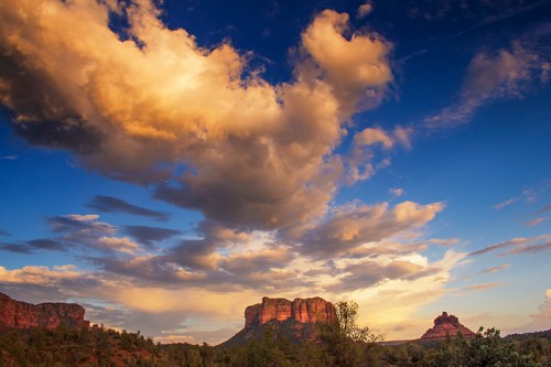 A scenic view of red rock formations under a vibrant sky with clouds at sunset.