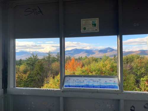 View from a lookout tower showing mountains and colorful trees under a blue sky with clouds. Information panel visible.