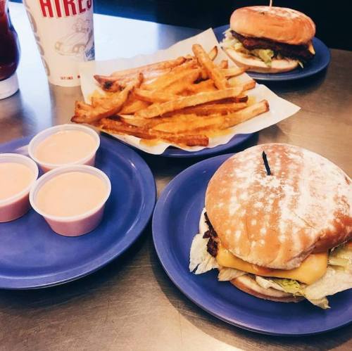 A plate with a cheeseburger, fries, and dipping sauces, alongside a drink in a fast-food setting.