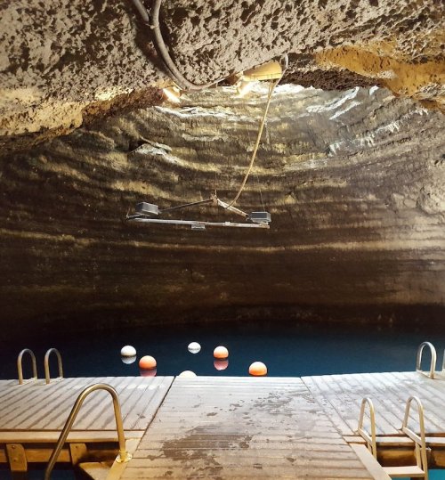 A dimly lit cave with a wooden platform and colorful buoys floating in the water below.