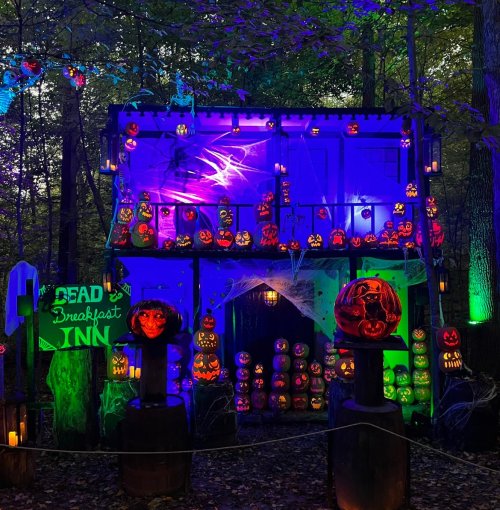 A spooky Halloween display featuring a haunted inn adorned with glowing jack-o'-lanterns and eerie lighting in a forest.