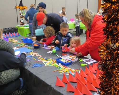 Children and adults engage in a craft activity at a table filled with colorful supplies and decorations.