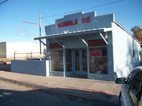 A blue storefront with "Humble Pie" sign and "OPEN" in red, featuring large windows and a sidewalk in front.