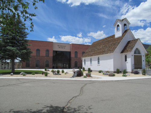 A small white church beside a modern museum building, set against a blue sky with scattered clouds.