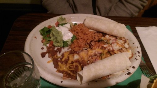 A plate of Mexican food featuring rice, beans, salad, sour cream, and two rolled tortillas.