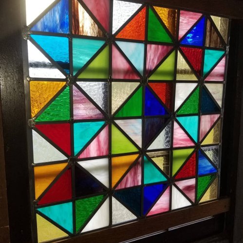 Colorful stained glass window featuring a geometric pattern of triangles and squares in various hues.