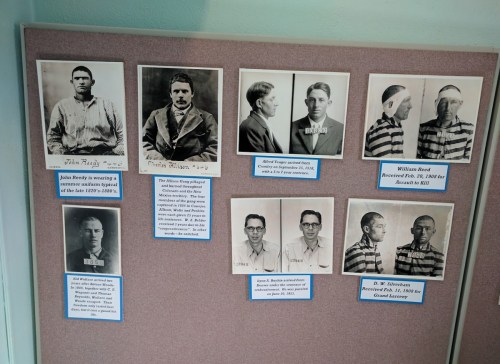 Historical mugshots of various individuals, each with a name and crime description, displayed on a bulletin board.