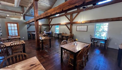 Cozy restaurant interior with wooden beams, tables, and chairs, featuring natural light from windows.