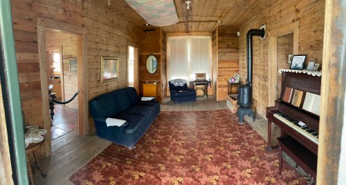 Cozy wooden room with a sofa, piano, and vintage decor, featuring a patterned rug and natural light.