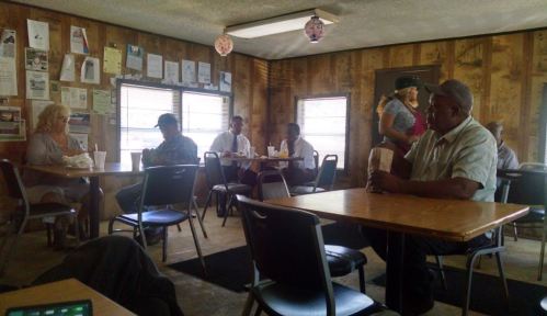 A cozy diner interior with several patrons seated at tables, some eating, and a server attending to customers.