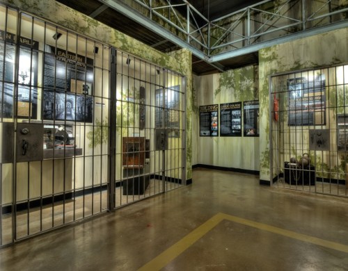 A dimly lit prison corridor with barred cells and informational displays on the walls.