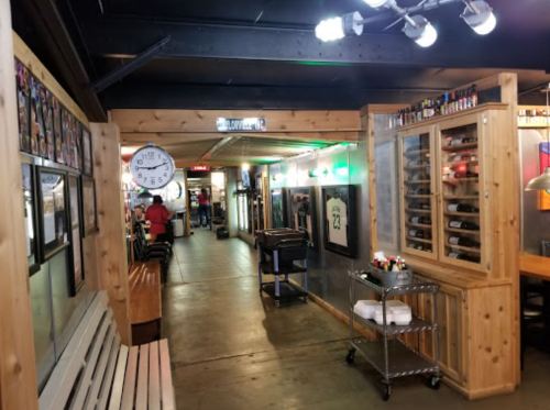 A wooden hallway in a restaurant with a clock, wine rack, and seating, leading to a dining area.