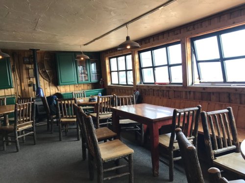 Cozy wooden dining area with tables and chairs, large windows, and warm lighting.