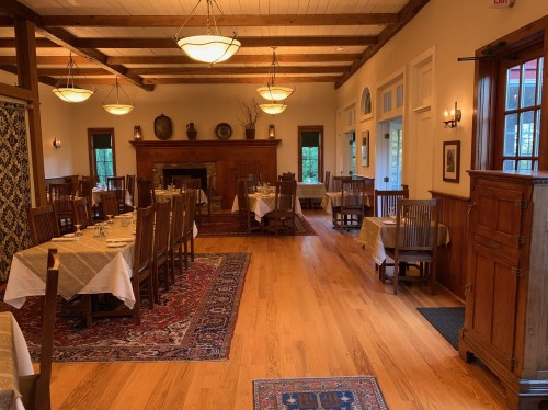Cozy dining room with wooden furniture, tables set with white tablecloths, and warm lighting.